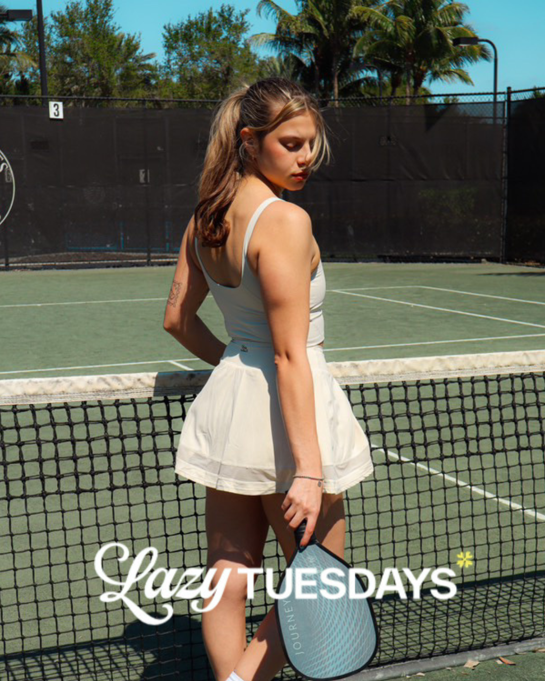 Lifestyle shot of a female athlete holding a tennis racket and dressed in a lazy Tuesday skirt and top